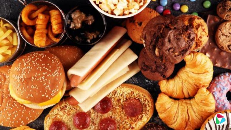 超级加工食品的俯视图,包括巧克力松饼、热狗、超市披萨、薯片、爆米花、甜甜圈、汉堡和糖果