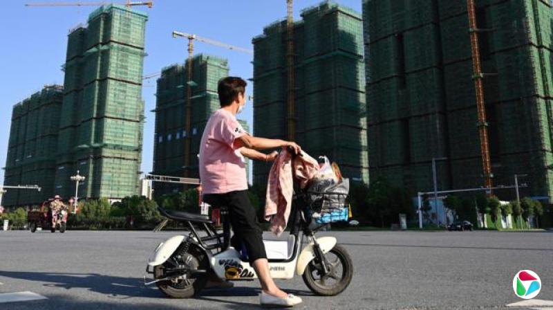 一名女子戴着口罩,身穿粉红色T恤(右袖上有米奇老鼠图案)和黑色长裤,骑着滑板车经过位于中国中部河南省驻马店市的恒大住宅建案施工现场。