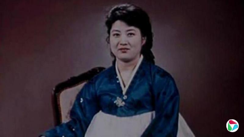 高英姬,大概三、四十岁,身穿蓝白相间的韩服,对着镜头微笑。
