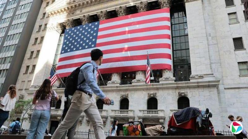 2026年5月26日早盘交易期间的纽约证券交易所(New York Stock Exchange)。大楼正面悬挂着一面巨大的美国国旗,街道上可见人们在其前方行走