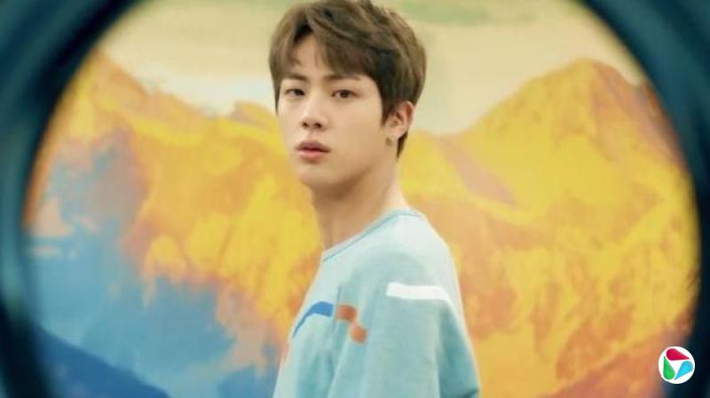 韩国流行音乐(K-pop)组合防弹少年团(BTS)的一名成员直视镜头,身后是泛黄的山脉。