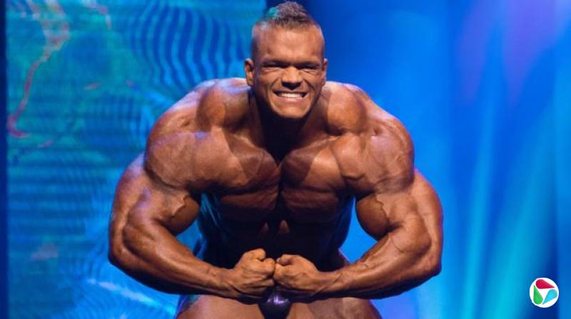 达拉斯·麦卡弗在阿诺德经典赛(Arnold Classic)台上摆出姿势,在蓝色背景前展示其肌肉极为发达的体格。